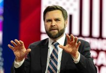 Man in suit gesturing with hands on stage.