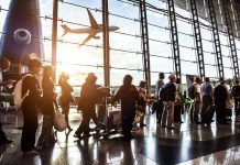 Crowd of travelers in airport terminal with airplane outside.
