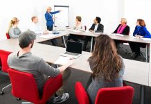 Hochul’s $500 Million Pension Gamble A diverse group of professionals engaged in a meeting with a presenter at a whiteboard