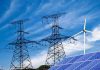 Data Center Boom, Or Grid Time Bomb? Power lines, solar panels, and wind turbine against sky.