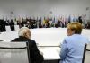 Mystery Iran Deal Stuns G7 People seated around a large round table, flags behind.