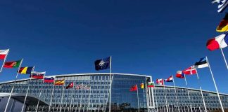 Europe’s Future? Americans Stuck With The Bill Flags outside NATO headquarters building under clear blue sky.