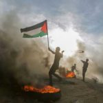 Protester waves a Palestinian flag amid smoke and fire