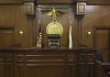 Six Months For Child Rape?! Judges bench in an empty courtroom, scales emblem above.