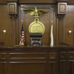 Judges bench in an empty courtroom, scales emblem above.