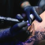 Tattoo artist with black gloves inking a detailed arm design