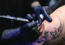 Tattoo Tax Panic Explodes Online Tattoo artist with black gloves inking a detailed arm design