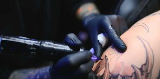 Tattoo Tax Panic Explodes Online Tattoo artist with black gloves inking a detailed arm design