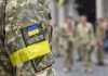 Protest Fury Forces Zelensky Shake-Up Soldier in camouflage with Ukrainian flag patch and yellow armband