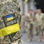 Protest Fury Forces Zelensky Shake-Up Soldier in camouflage with Ukrainian flag patch and yellow armband
