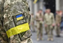 Protest Fury Forces Zelensky Shake-Up Soldier in camouflage with Ukrainian flag patch and yellow armband
