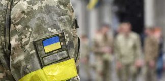Protest Fury Forces Zelensky Shake-Up Soldier in camouflage with Ukrainian flag patch and yellow armband