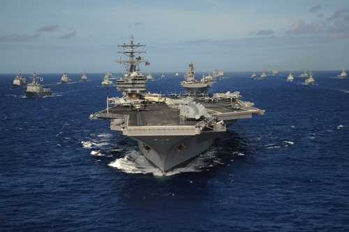 shutterstock_2599523537 An aircraft carrier surrounded by a fleet of naval ships in the ocean