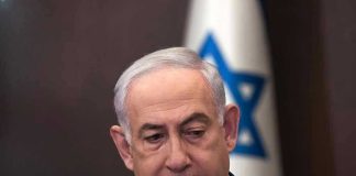 Is Iran Targeting Netanyahu’s SON?! Man in suit with Israeli flag in background.