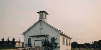 Small white church with steeple and cross at sunset