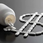 White pills forming a dollar sign beside a spilled pill bottle