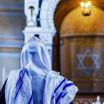 Man Attacks Jewish Worshippers Inside NYC Synagogue Person in white and blue prayer shawl facing ornate interior