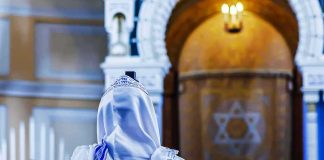Person in white and blue prayer shawl facing ornate interior