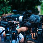 DHS Blames Biden For Preventable Killing TV news cameras crowding together at an outdoor event