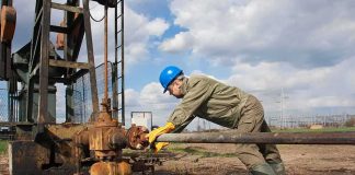 Cyberattack HITS Oil Tanker Headed for Texas Worker in blue hard hat operating rusty oil pump equipment outdoors
