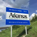 Arkansas welcome sign by a highway with grass and cloudy sky
