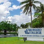 Broward College campus sign by palm trees and pond