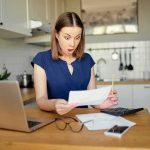 This State Wants to Add ‘JEWISH’ to State Forms Woman in kitchen reacting to a bill at a table with laptop and calculator
