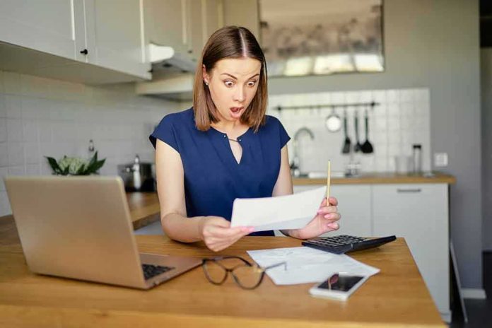 shutterstock_1160548099 Woman in kitchen reacting to a bill at a table with laptop and calculator