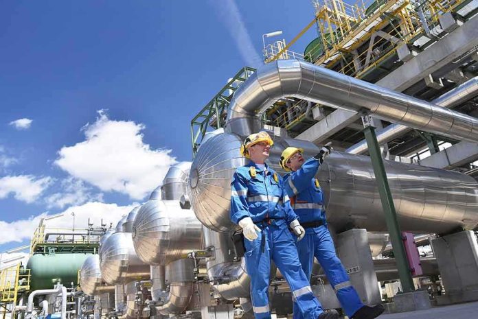 Two industrial workers walking under large metal pipes