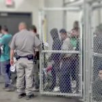 Governor vs. DHS: Who’s Hiding Newark? People standing inside chain-link holding area with an officer nearby