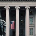 Trump Blocks Permanent Pick For National Intelligence Spot Statue in front of a neoclassical government building with columns and a U.S. flag