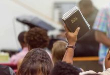 Iran War Is SPLITTING Trump’s Christian Base Hand holding a Bible in a crowded church service
