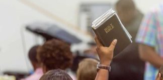 Iran War Is SPLITTING Trump’s Christian Base Hand holding a Bible in a crowded church service