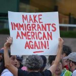 Senator Hit by Pepper Spray in Chaos Teddy Williams at a protest holding a sign reading 'Make Immigrants American Again'