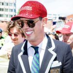 DOJ’s $1.8B Bombshell Freezes Mid-Flight Man in red sequined cap smiling at an outdoor crowd