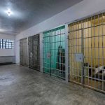 ICE Expansions: Bed Crunch Chokes Deportations Interior view of a prison cell block with metal bars and concrete flooring