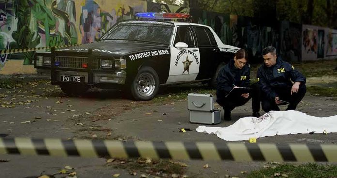 shutterstock_1709493973 Crime scene with police car and two investigators by a covered body
