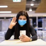 UK Ban Could Muzzle Everyone Woman in face mask video calling on smartphone in a cafeteria