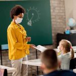 Teacher REPRIMANDED for Wearing ‘XX=XY’ Shirt Teacher in yellow shirt handing paper to student in classroom