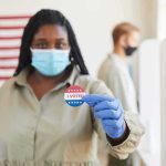 Dem Civil War Over Black Votes Voter wearing a mask holds an I Voted sticker at a polling place