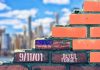 9/11 Didn’t End—It Rewired America Brick wall with American flag and memorial text against city skyline