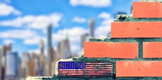 9/11 Didn’t End—It Rewired America Brick wall with American flag and memorial text against city skyline
