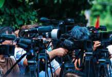 DHS Blames Biden For Preventable Killing TV news cameras crowding together at an outdoor event