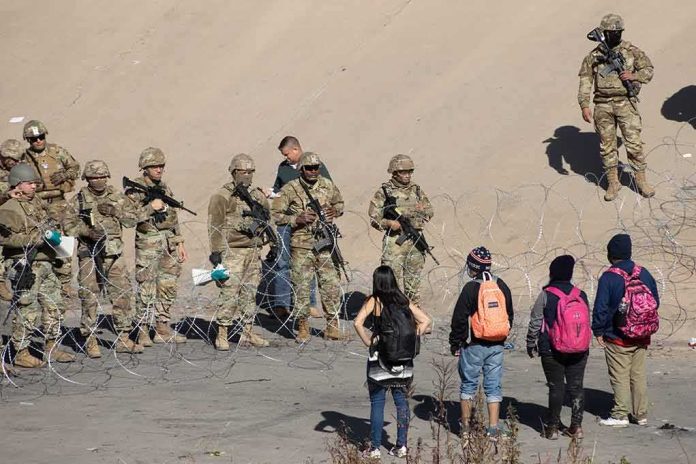 shutterstock_2257546051 Soldiers stand behind barbed wire facing civilians