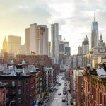 Mamdani Aide Calls Seizing Homes a ‘Sacred Right’ City street leading to a skyline of modern and historic skyscrapers at sunset