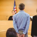 Impersonated Cop, Then This Defendant in handcuffs standing before a judge in a courtroom