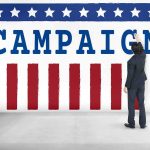Cruz Drops $1.7M ‘LifeLine’ to Save Paxton Man in suit writing on large campaign banner with stars and stripes