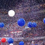 Blue and white balloons with confetti falling over a crowded indoor arena