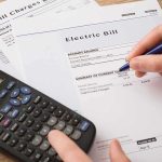 80% Higher Power Bills? There’s More to It hand reviewing utility bills with calculator on desk