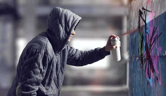 shutterstock_556304779 Person in hoodie spray painting a wall